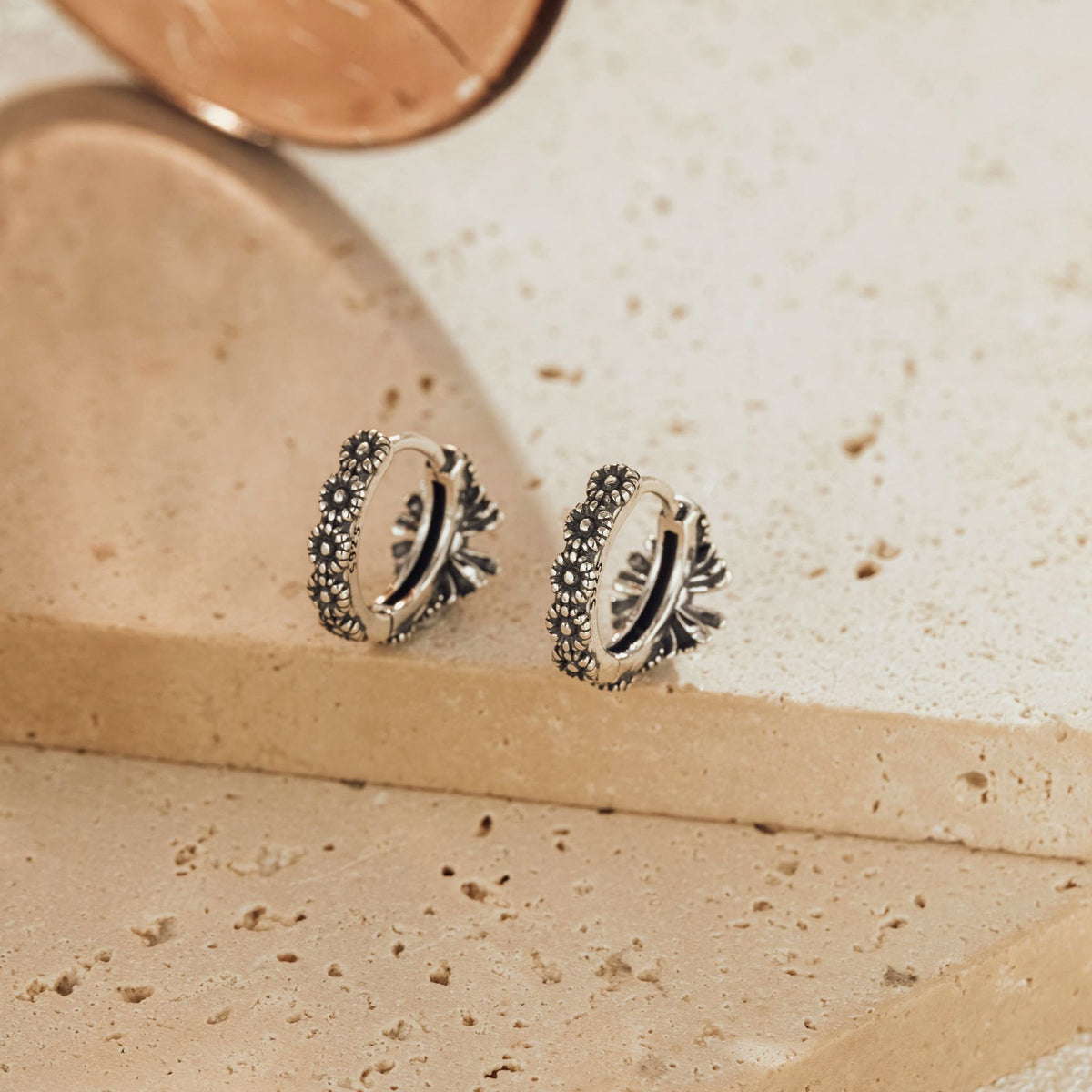 Pair of oxidized sterling silver sunflower huggie earrings standing upright, side profile view