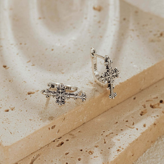 Close-up of sterling silver Gothic cross huggie earrings on textured stone
