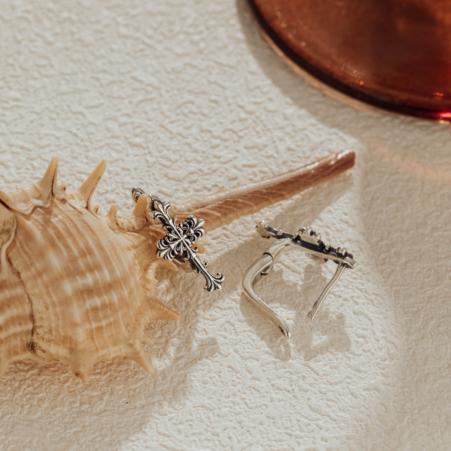 Silver Gothic cross huggie earrings displayed with seashell background