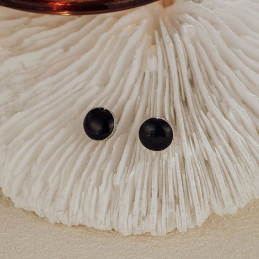 Minimalist sterling silver and black CZ stud earrings styled on shell