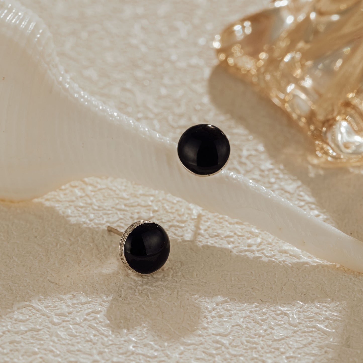 Pair of black cubic zirconia stud earrings displayed on coral stone