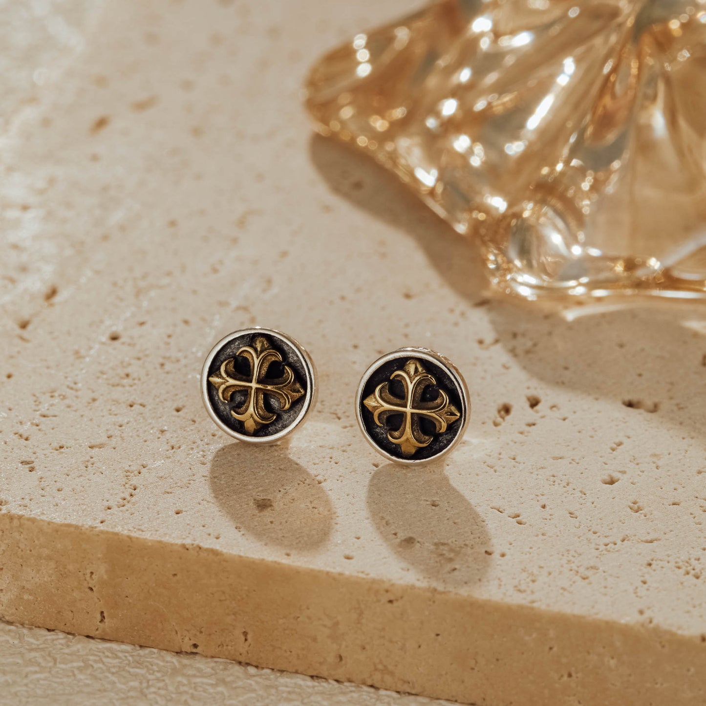 Pair of mini cross medallion two-tone sterling silver stud earrings on stone background