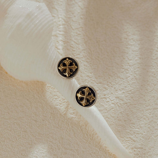 Close-up of small cross medallion stud earrings displayed on a seashell