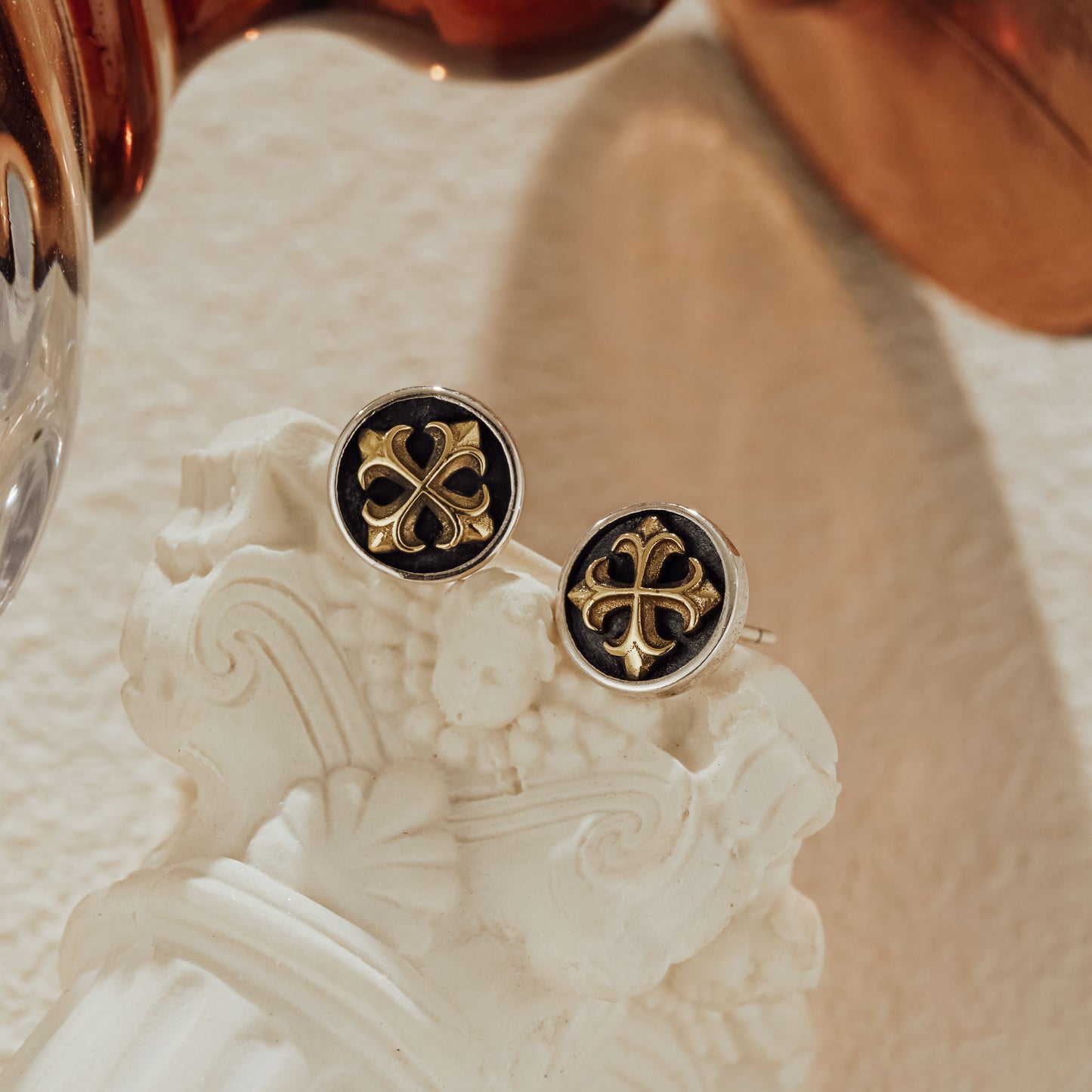 Two-tone cross stud earrings styled on a classical white column accent