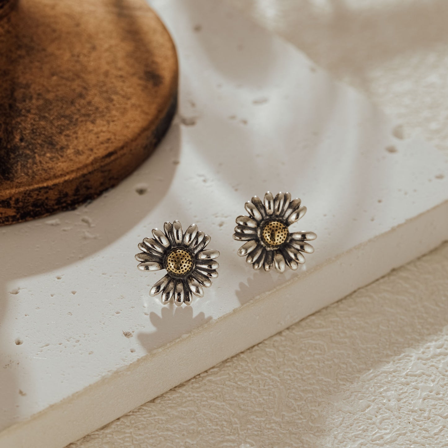 Close-up of daisy stud earrings placed on textured stone surface