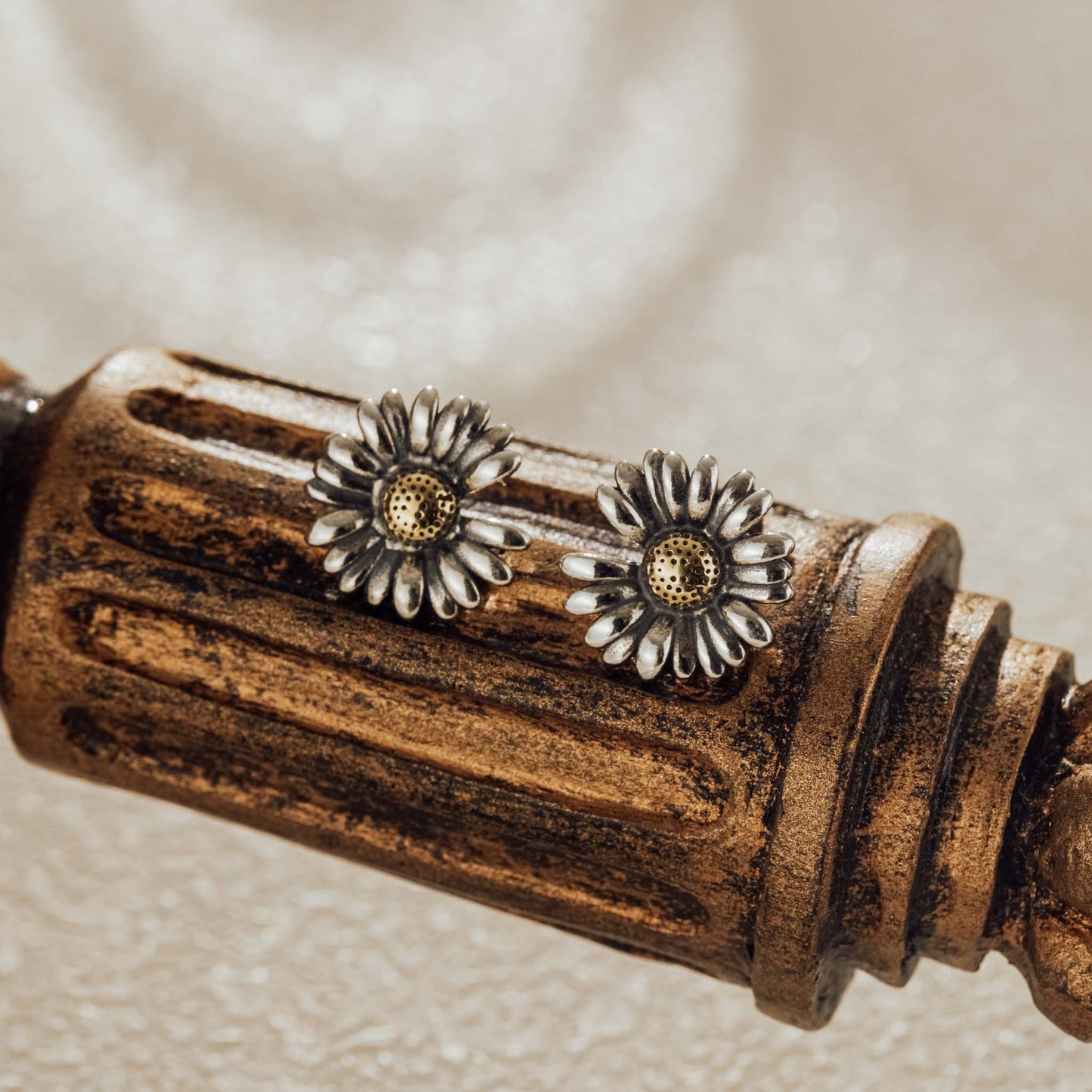 Vintage-style daisy silver earrings displayed on a rustic wooden accent