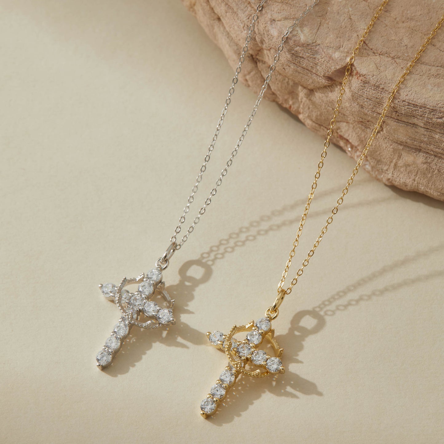 Gold and silver rotatable crown cross necklaces on neutral background
