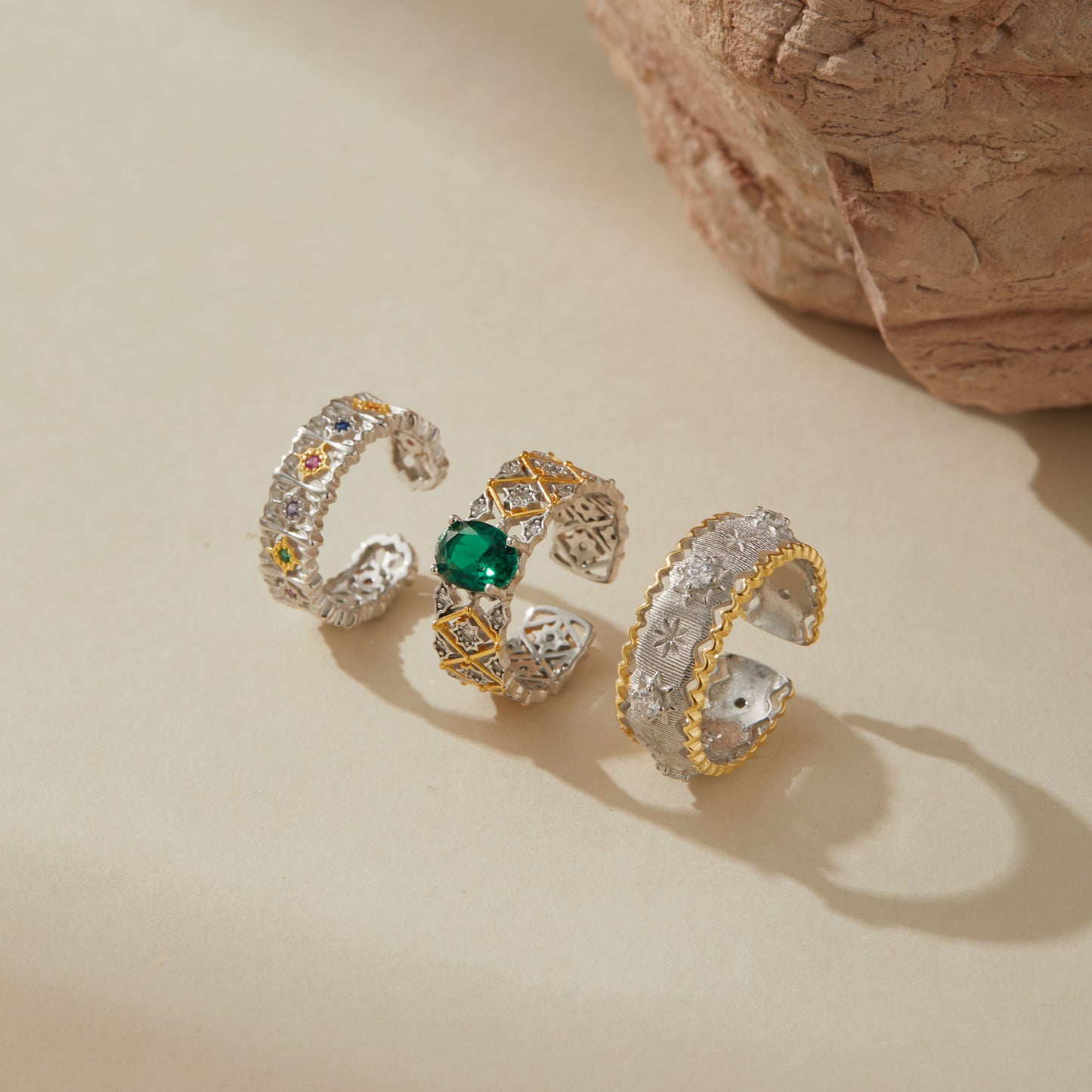 Three sterling silver adjustable rings with crystal accents — floral multicolor ring, emerald green gemstone ring with gold accents, and silver starburst ring with gold edge