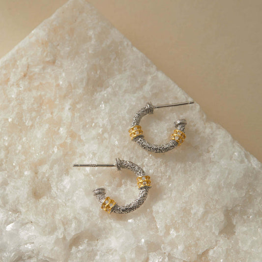 Sterling silver engraved hoop earrings with gold-tone accents, displayed on crystal stone