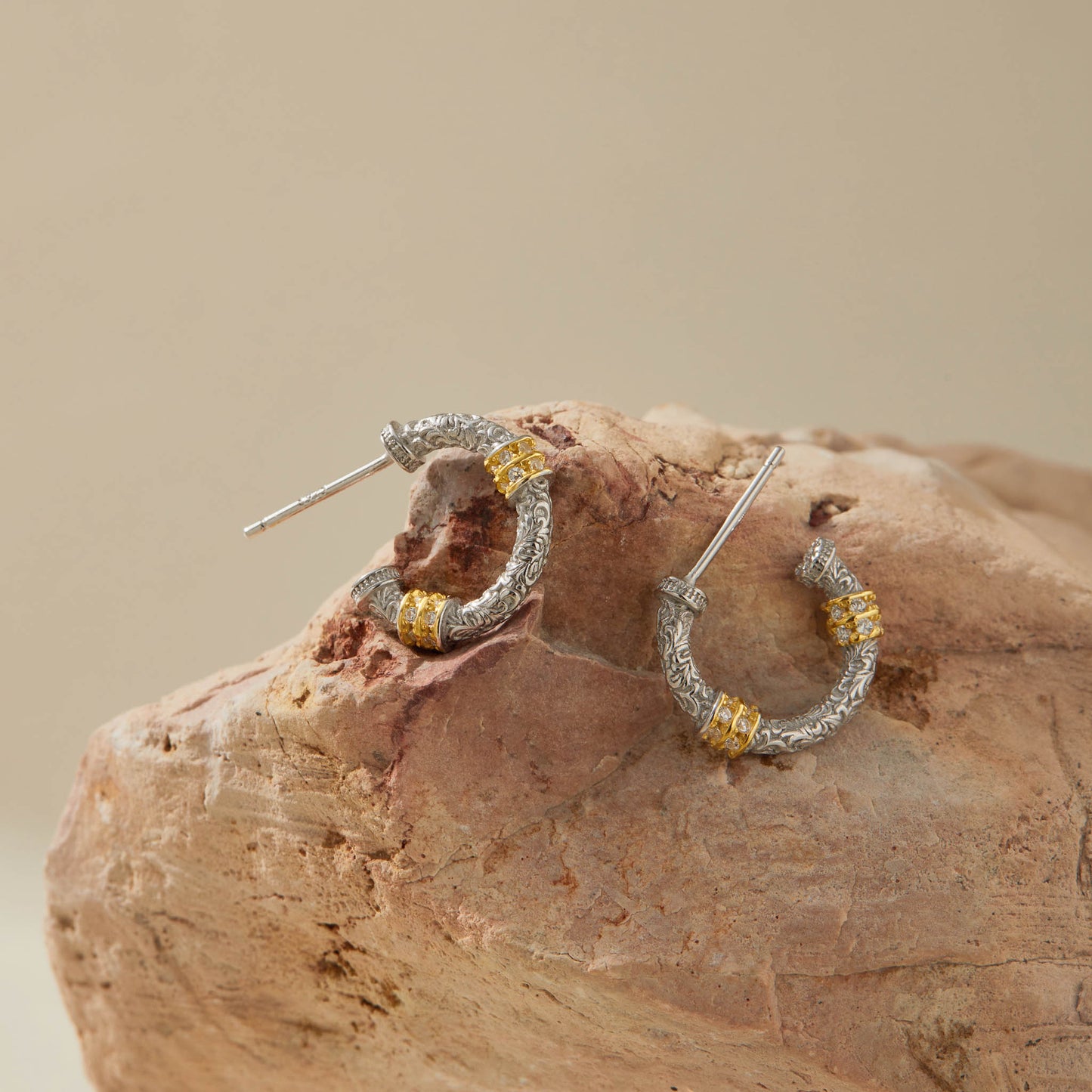 Small engraved silver hoop earrings with gold details, displayed on stone