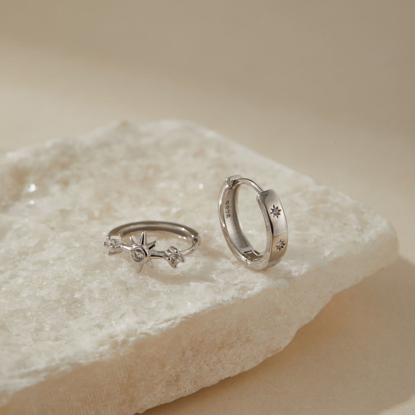 Asymmetric sterling silver starburst huggie earrings styled on white stone