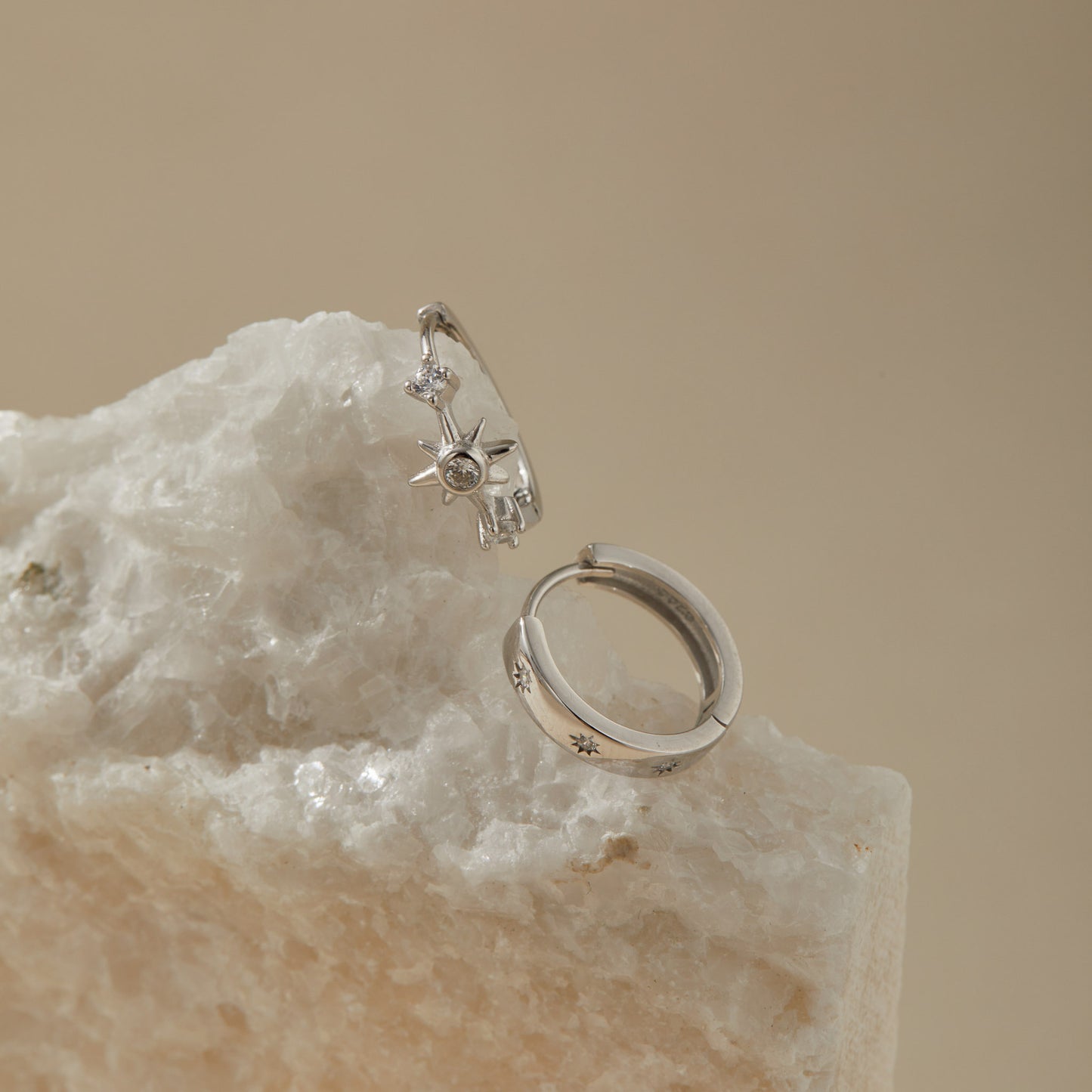 Starburst huggie earring set on quartz surface, polished sterling silver