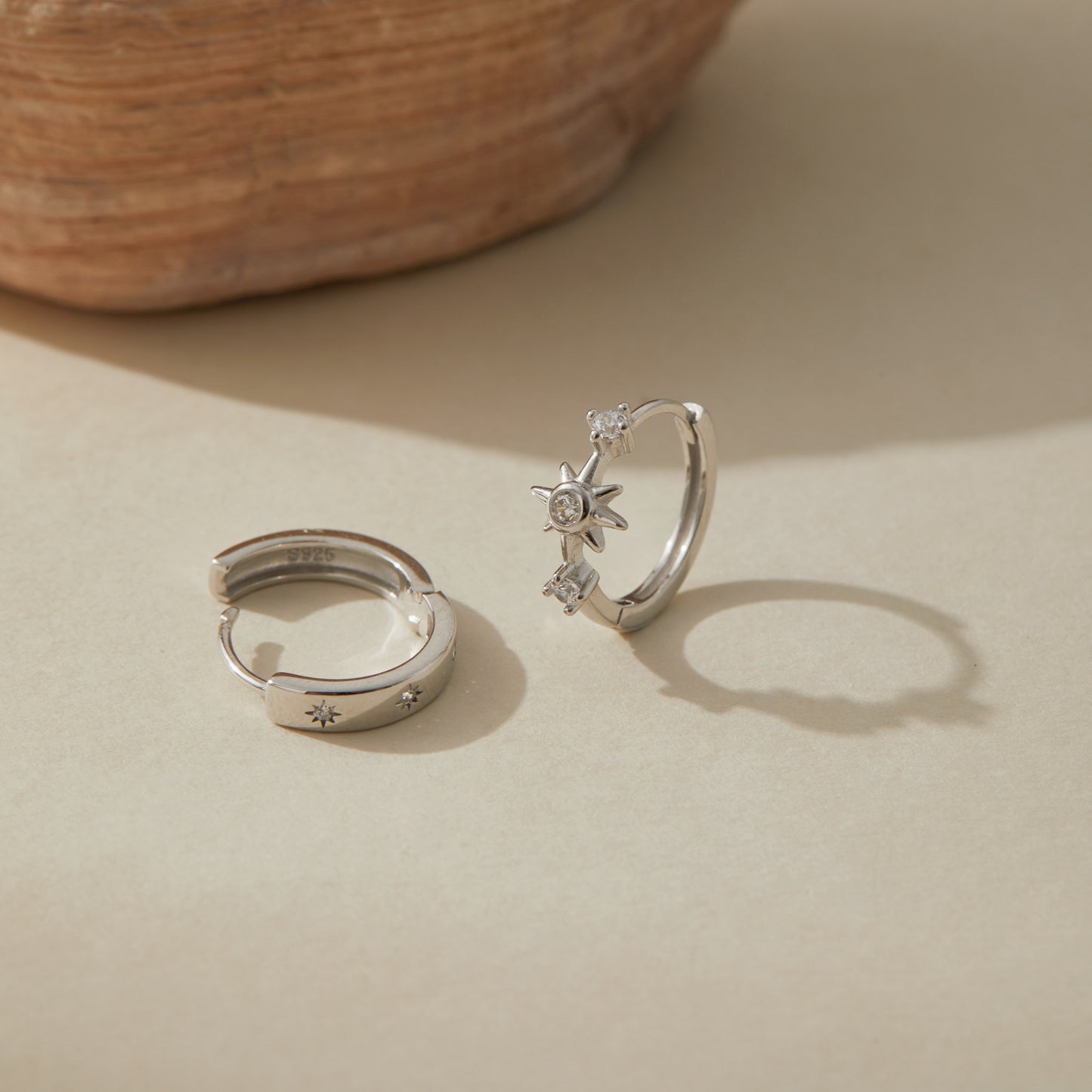Pair of sterling silver huggie earrings, one with cubic zirconia starburst, one engraved with star motifs