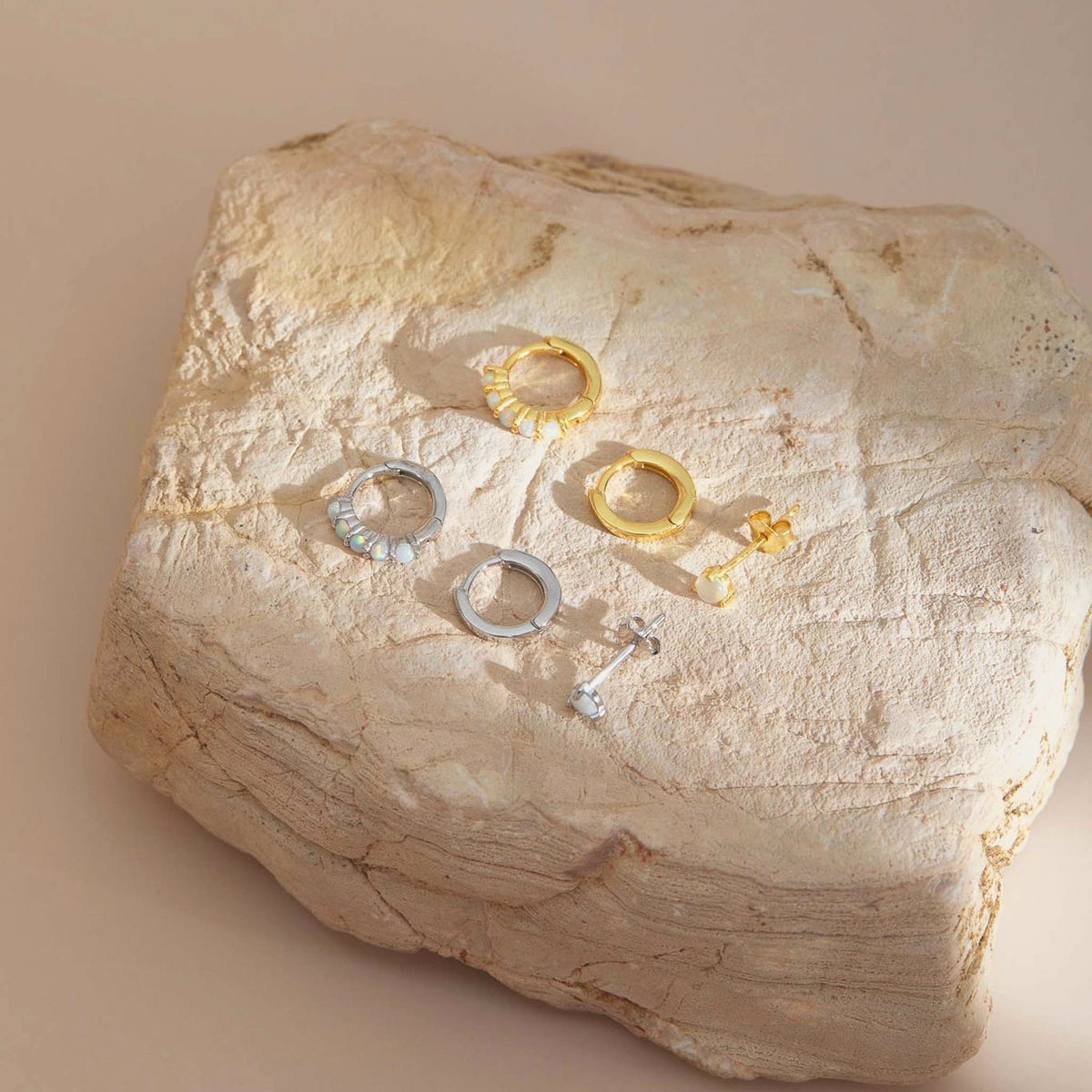 Gold plated and sterling silver opal earring sets of three, huggies, plain hoops and studs, on a pale stone block