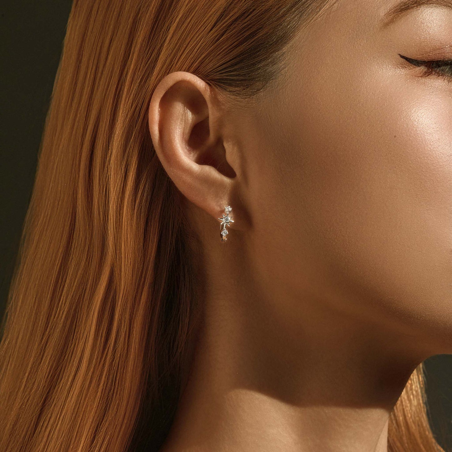 Lifestyle photo – asymmetric starburst huggie earrings worn on ear
