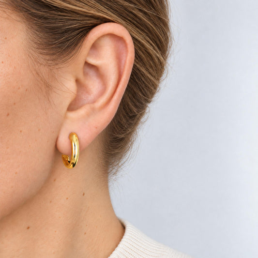 Woman wearing a gold-plated tapered huggie hoop on her earlobe, side view in an ivory knit