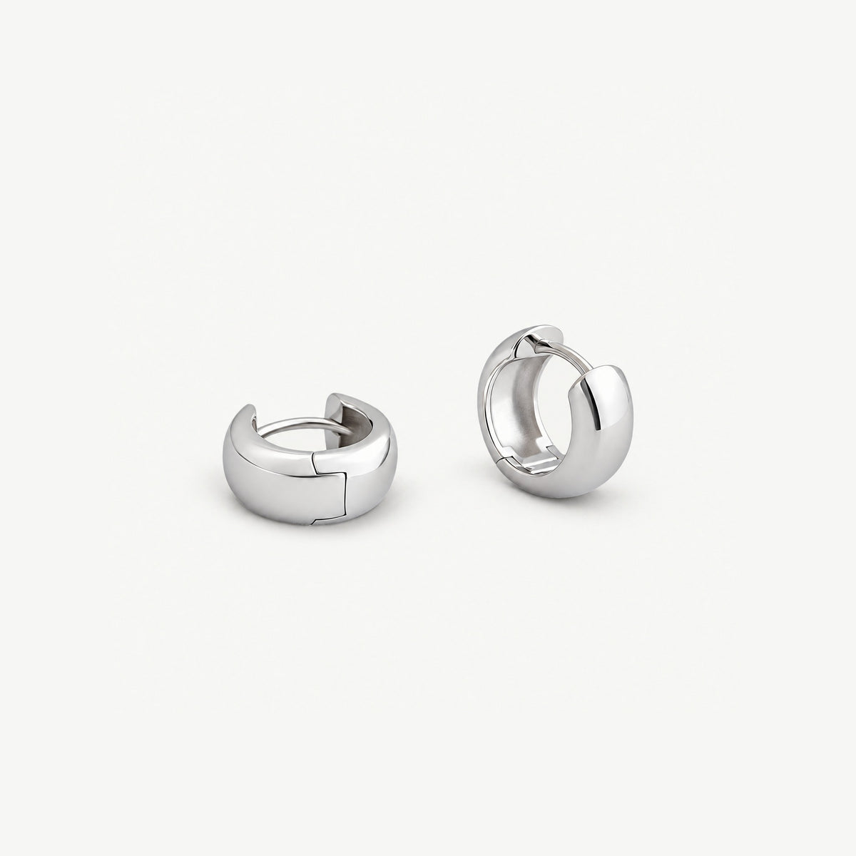 Chunky dome huggie hoops in white gold-plated silver, one showing its stepped hinge seam, one turned to the inside