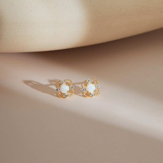 Gold S925 floral opal stud earrings resting on a soft neutral surface