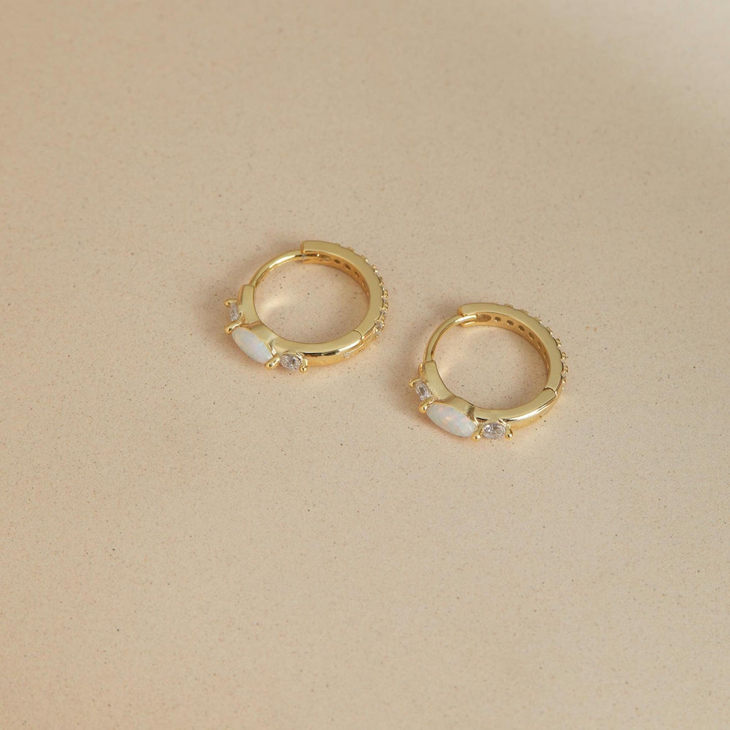 Gold opal and CZ huggie hoop earrings on neutral background