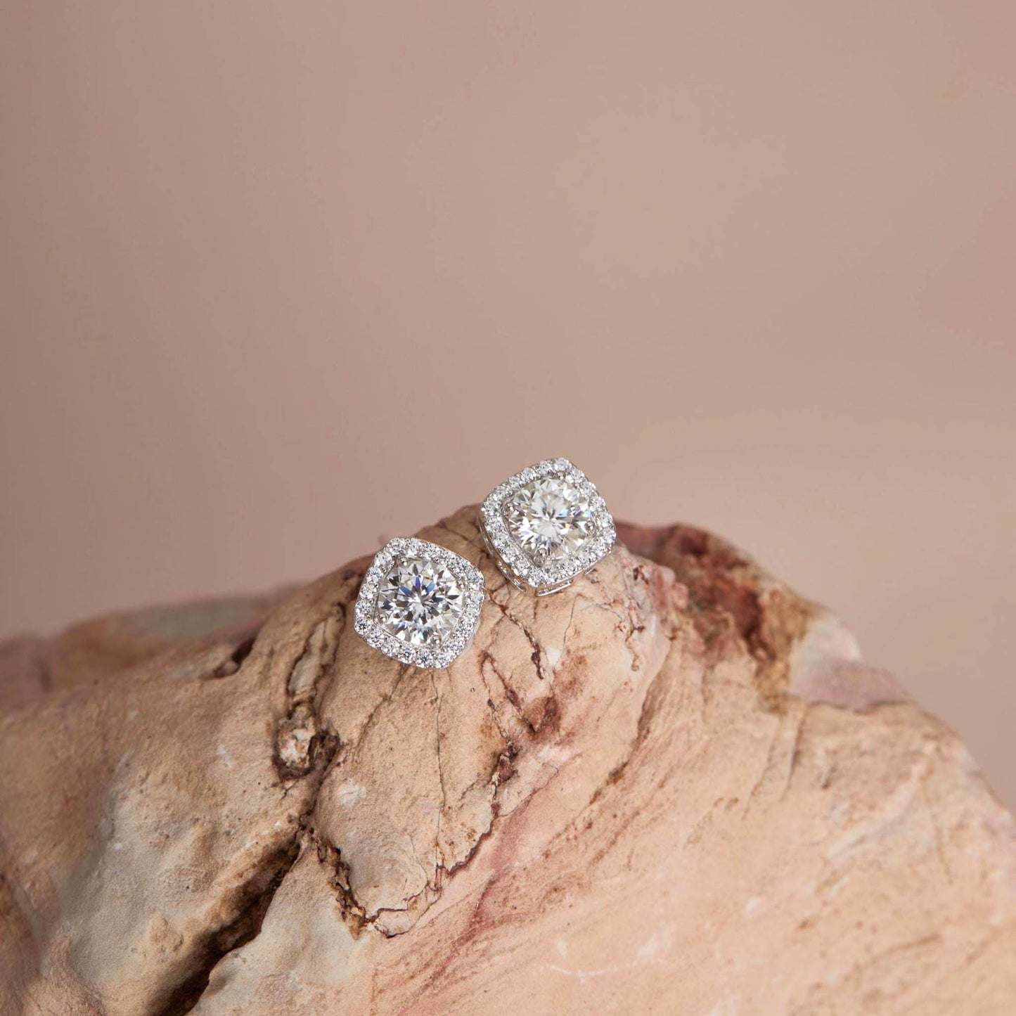 Flat lay on rock — White moissanite halo stud earrings, cushion setting.