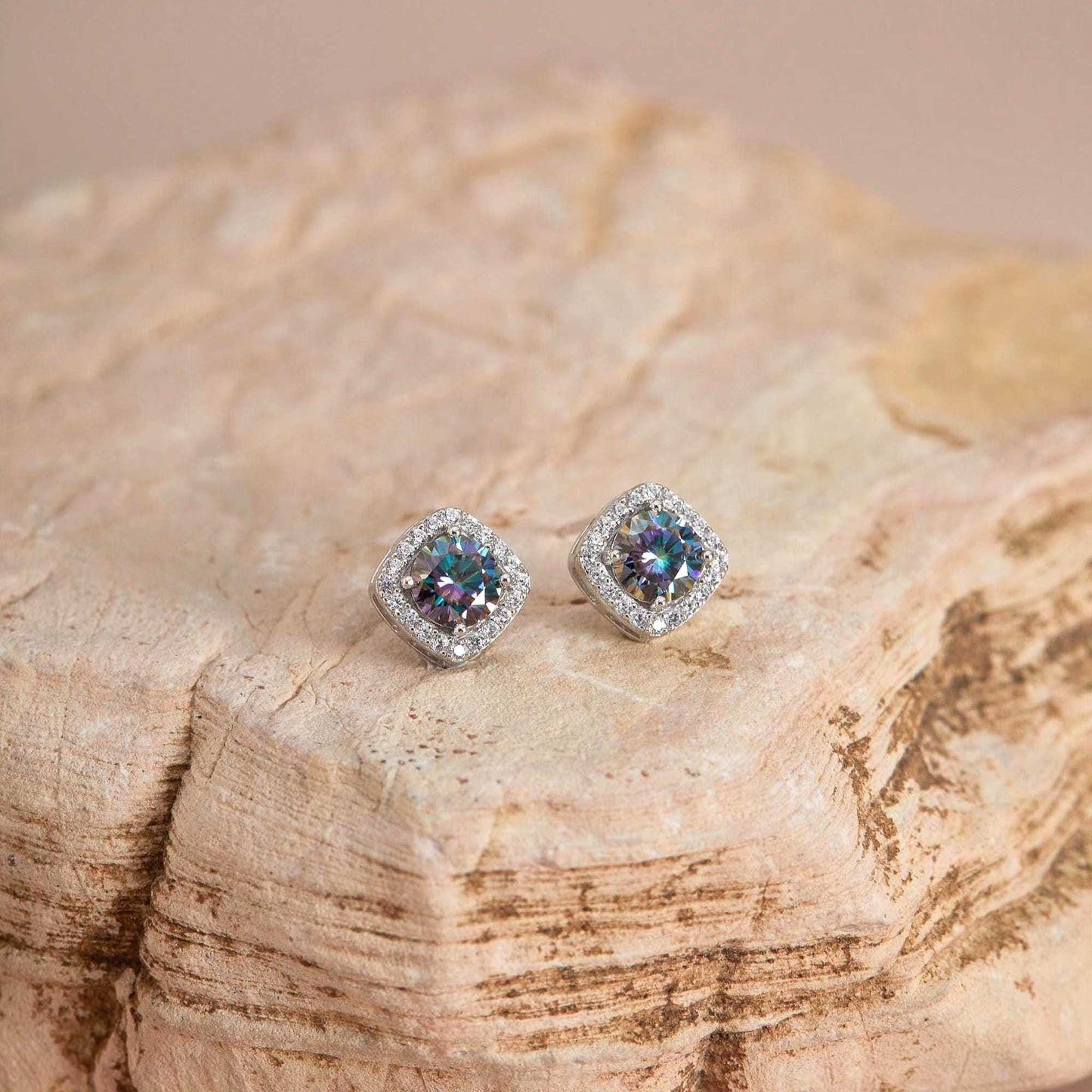 Flat lay on stone — Rainbow blue moissanite halo studs, cushion setting.