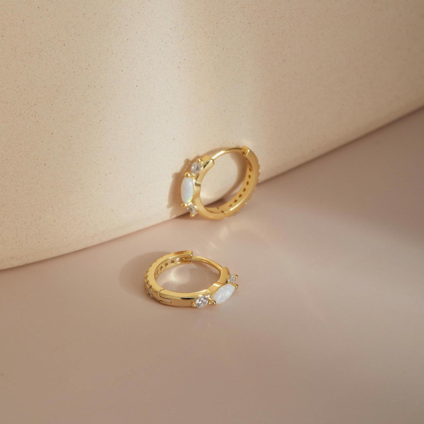 Gold opal huggie hoop earrings styled against soft backdrop