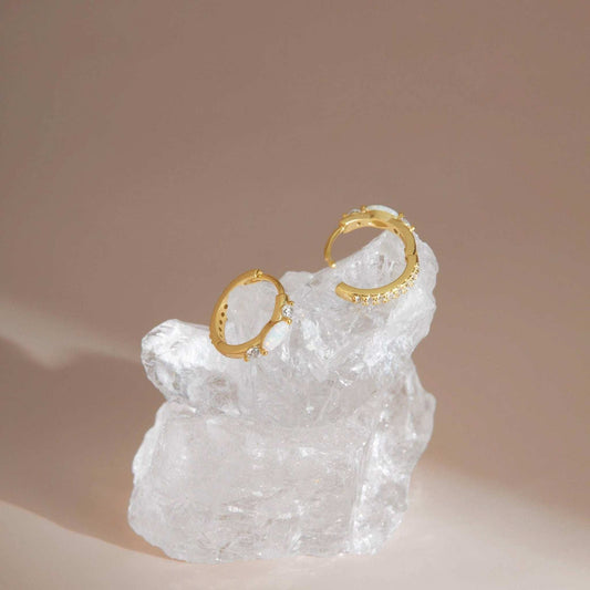 Gold opal huggie earrings on crystal prop