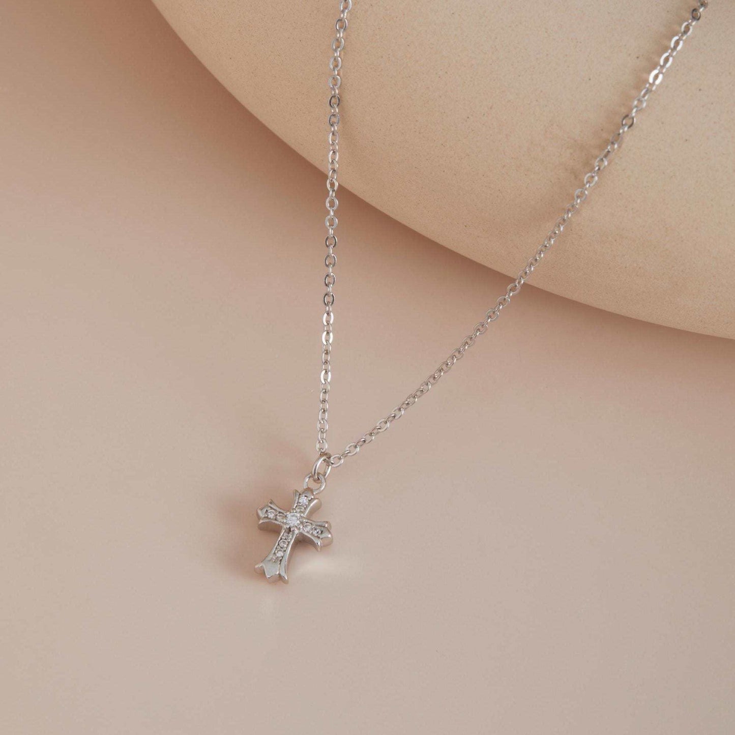 Silver cross necklace on a soft pink background