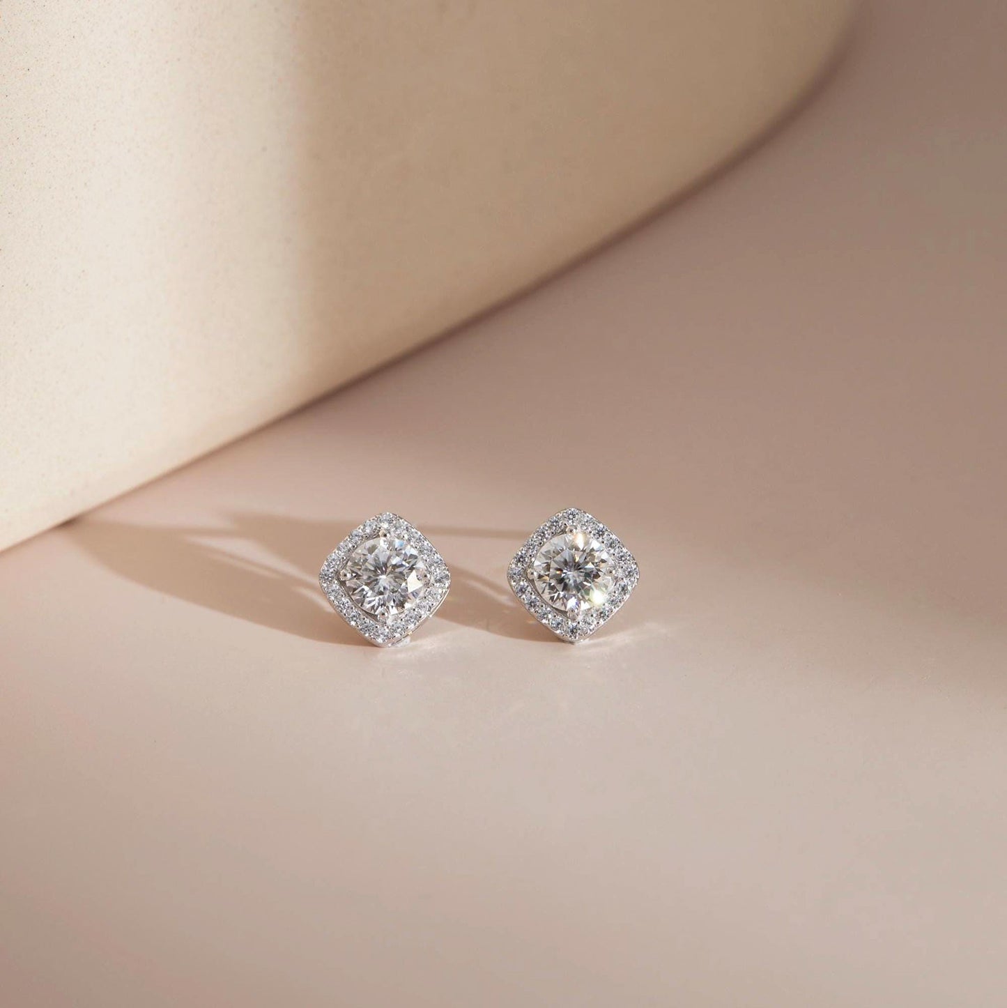 Flat lay on neutral surface — White moissanite halo stud earrings, sterling silver.