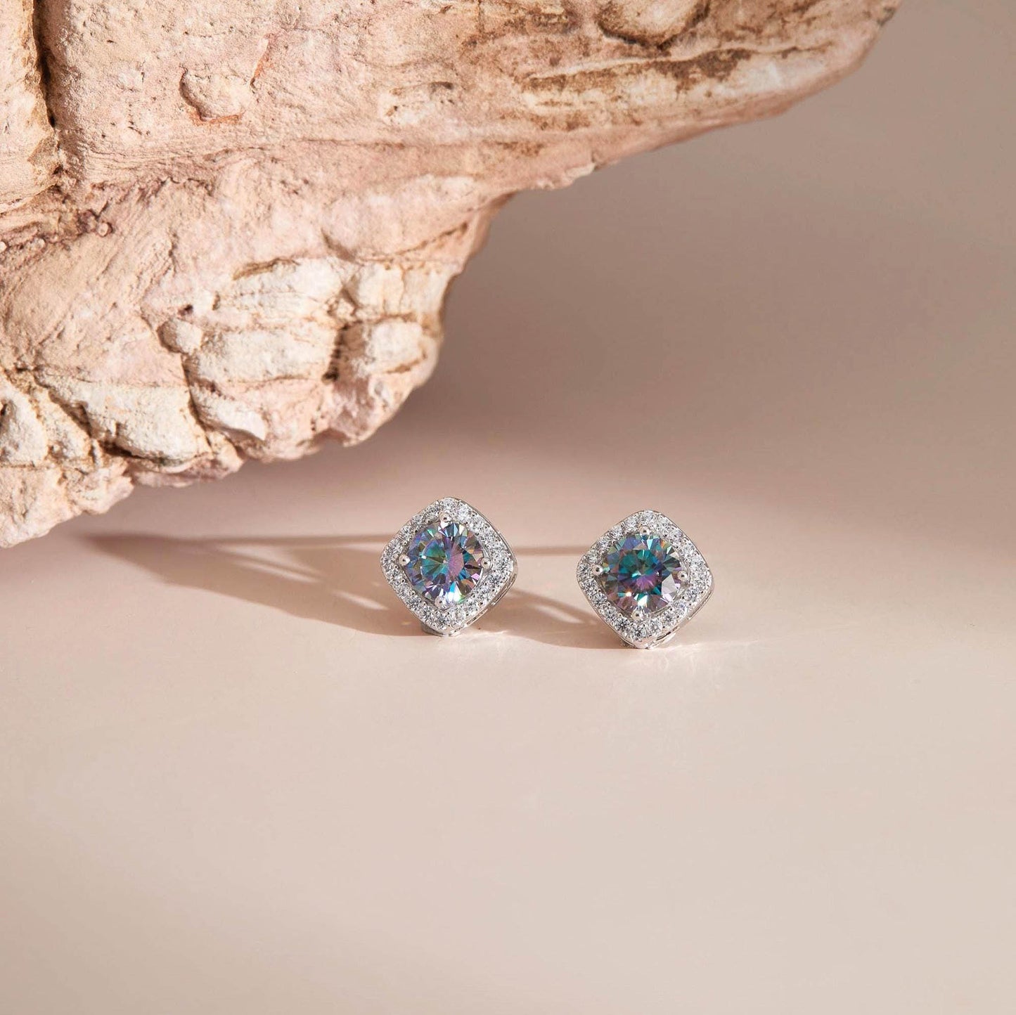 Flat lay on neutral surface — Rainbow blue moissanite halo stud earrings with sparkle.