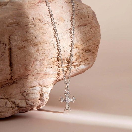 Silver necklace with a cross pendant on a stone surface