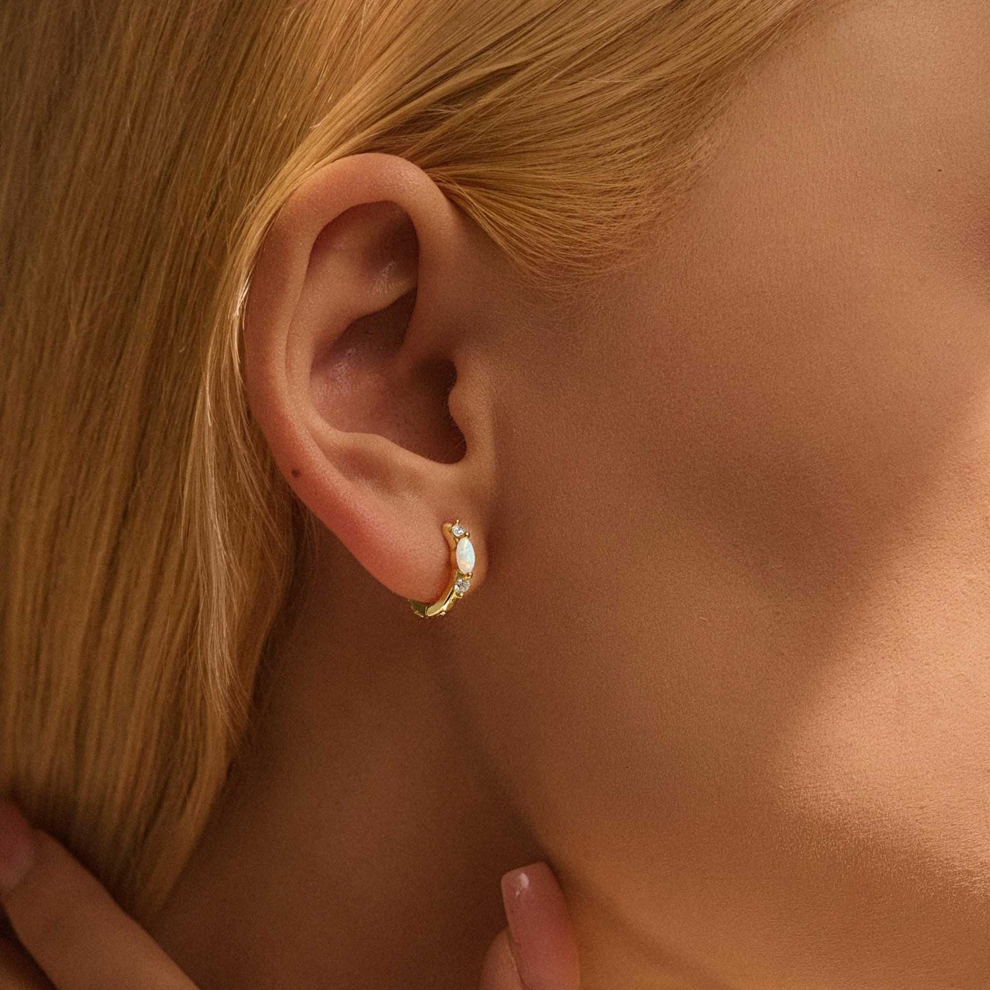Model wearing gold opal huggie hoop earrings
