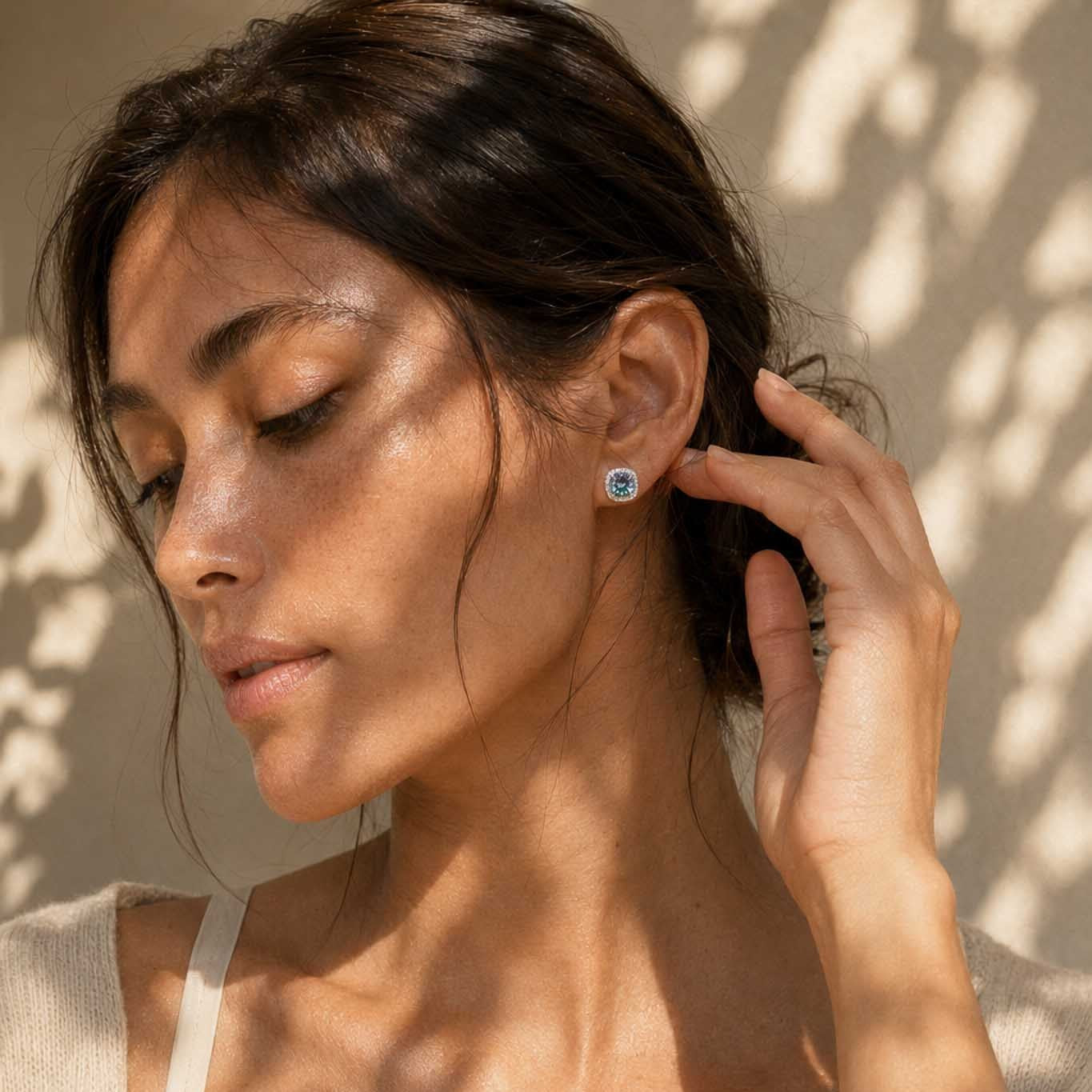 Woman wearing 1ct round cut rainbow blue moissanite halo stud earring in sterling silver, dappled light