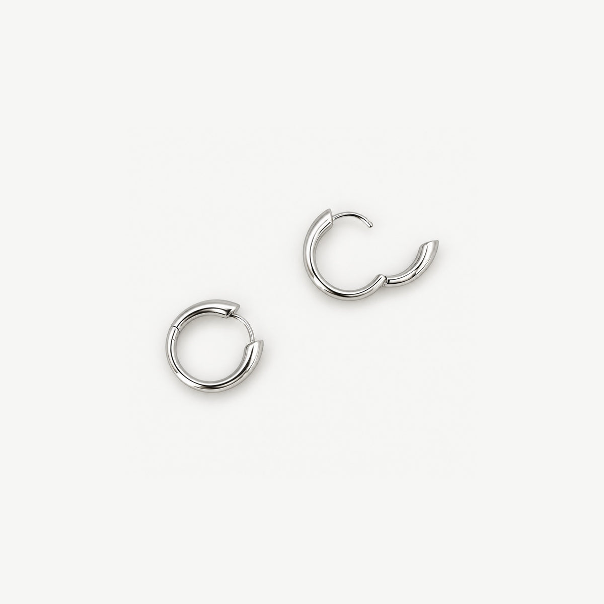 Top view of sterling silver huggie hoops, one snapped shut and one hinged open with its fine clicker wire showing