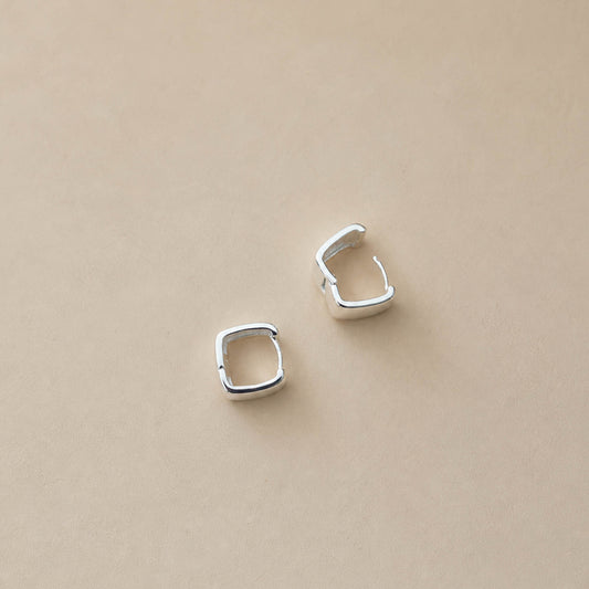 Pair of sterling silver chunky square huggie hoop earrings on cream backdrop, polished mirror finish