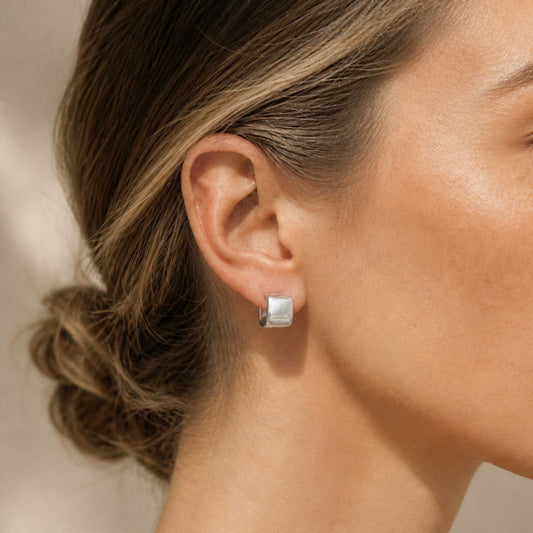 Woman wearing sterling silver chunky square huggie hoop earring, side profile with hair pulled back