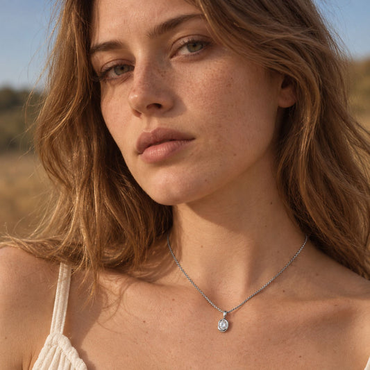 Woman with long wavy hair in a white crochet top wearing a dainty silver tone oval pendant necklace on her chest