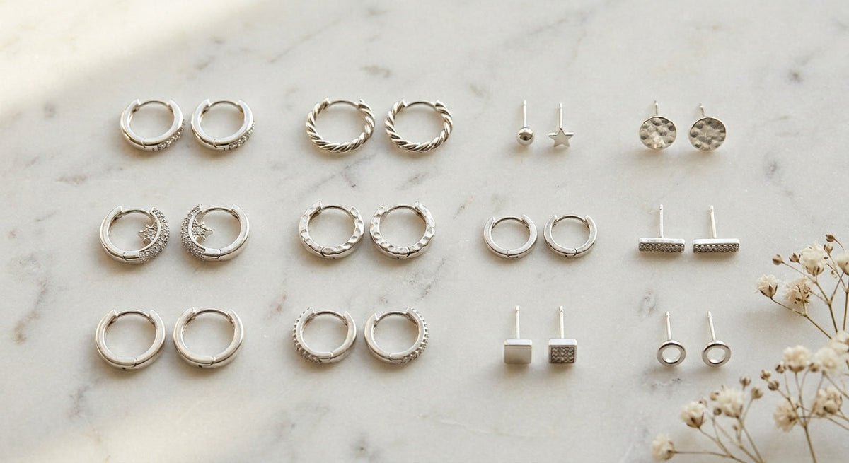 Flat lay of 925 sterling silver huggie earrings and stud earrings arranged on white marble with dried white flowers, soft natural lighting