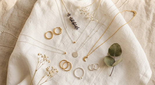 Hypoallergenic sterling silver jewelry pieces including earrings necklace and ring arranged on white linen with dried botanicals