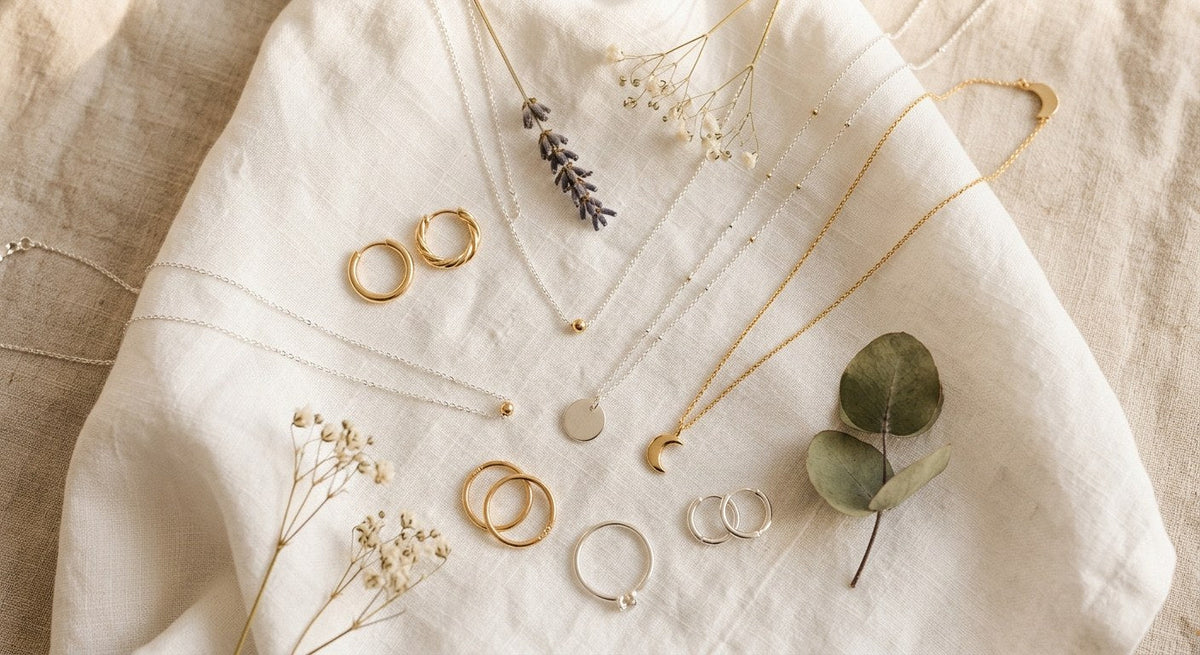 Hypoallergenic sterling silver jewelry pieces including earrings necklace and ring arranged on white linen with dried botanicals