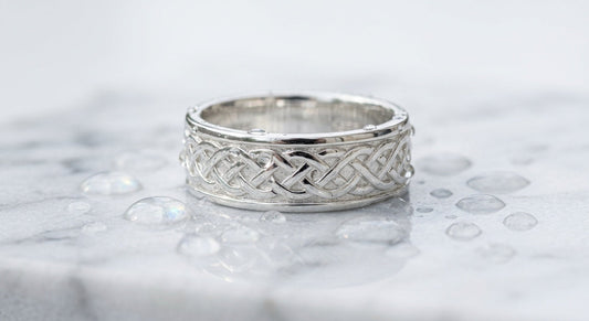 Polished sterling silver ring with intricate pattern on wet marble surface with water droplets, soft light