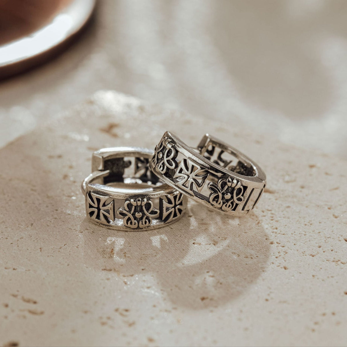 Pair of oxidized sterling silver gothic huggie earrings showing heraldic cross and fleur-de-lis engraving