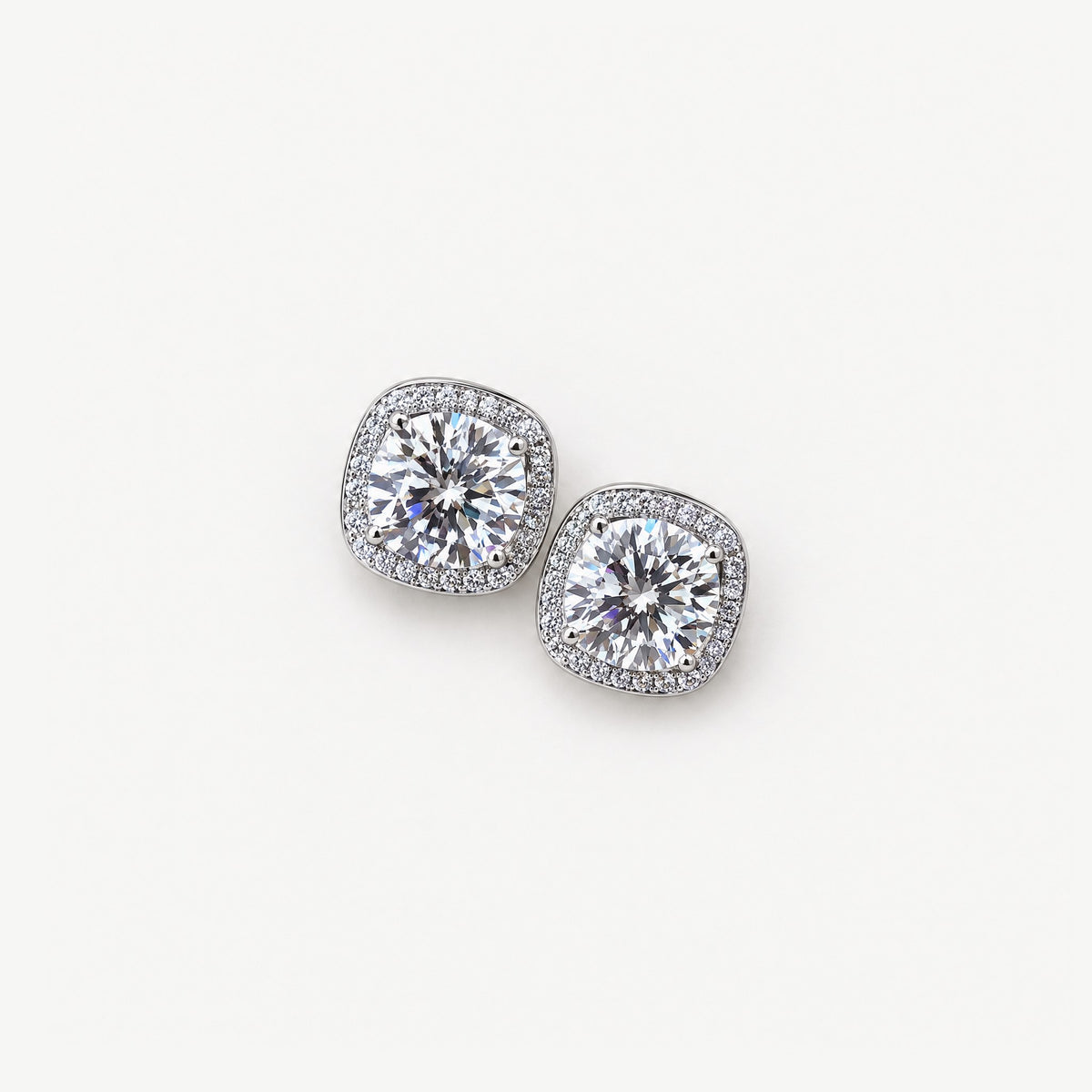 Pair of white 1ct round moissanite stud earrings with cushion-shaped pavé halos in sterling silver, from above