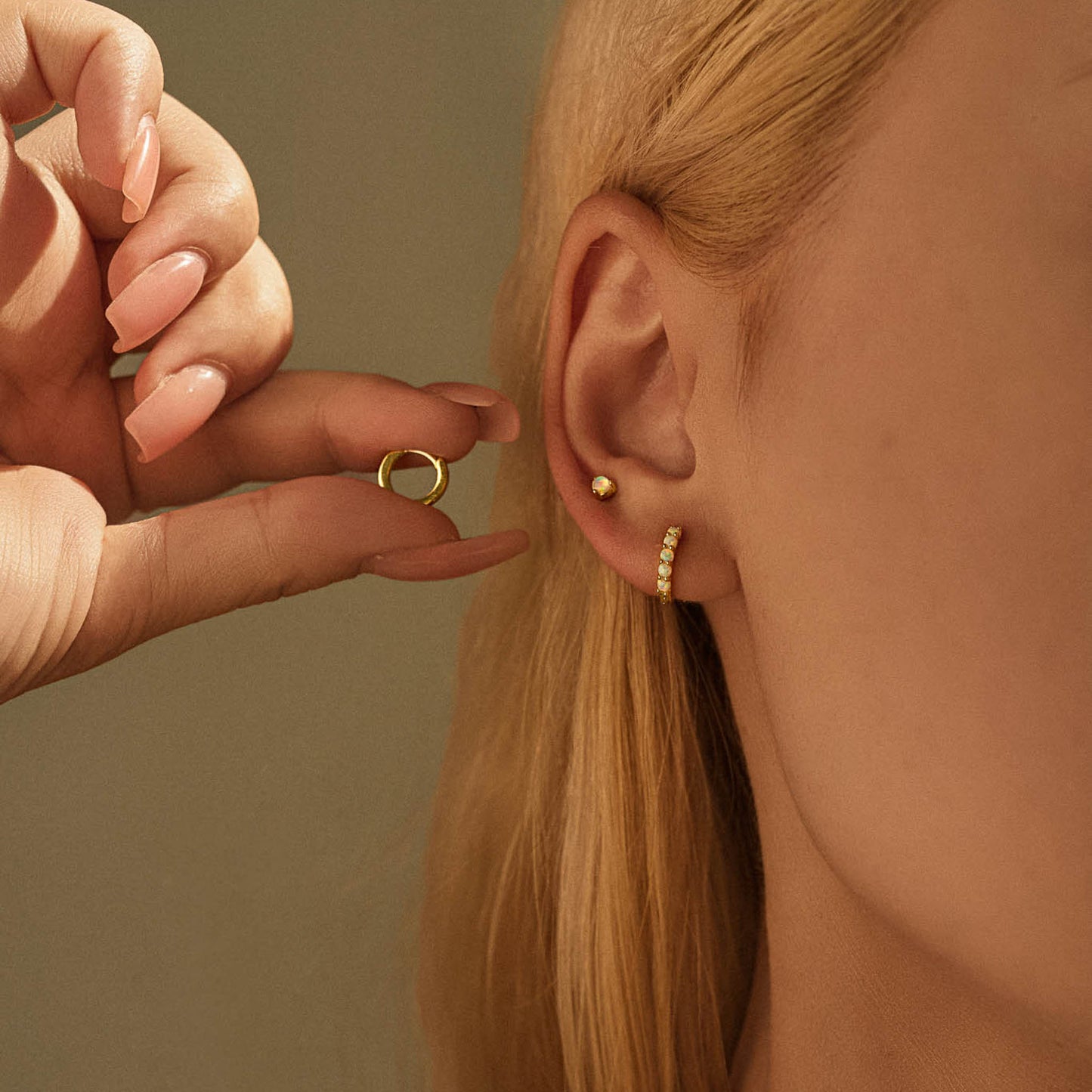 Model wearing gold plated opal stud and opal huggie hoop in a stacked ear, holding the plain huggie