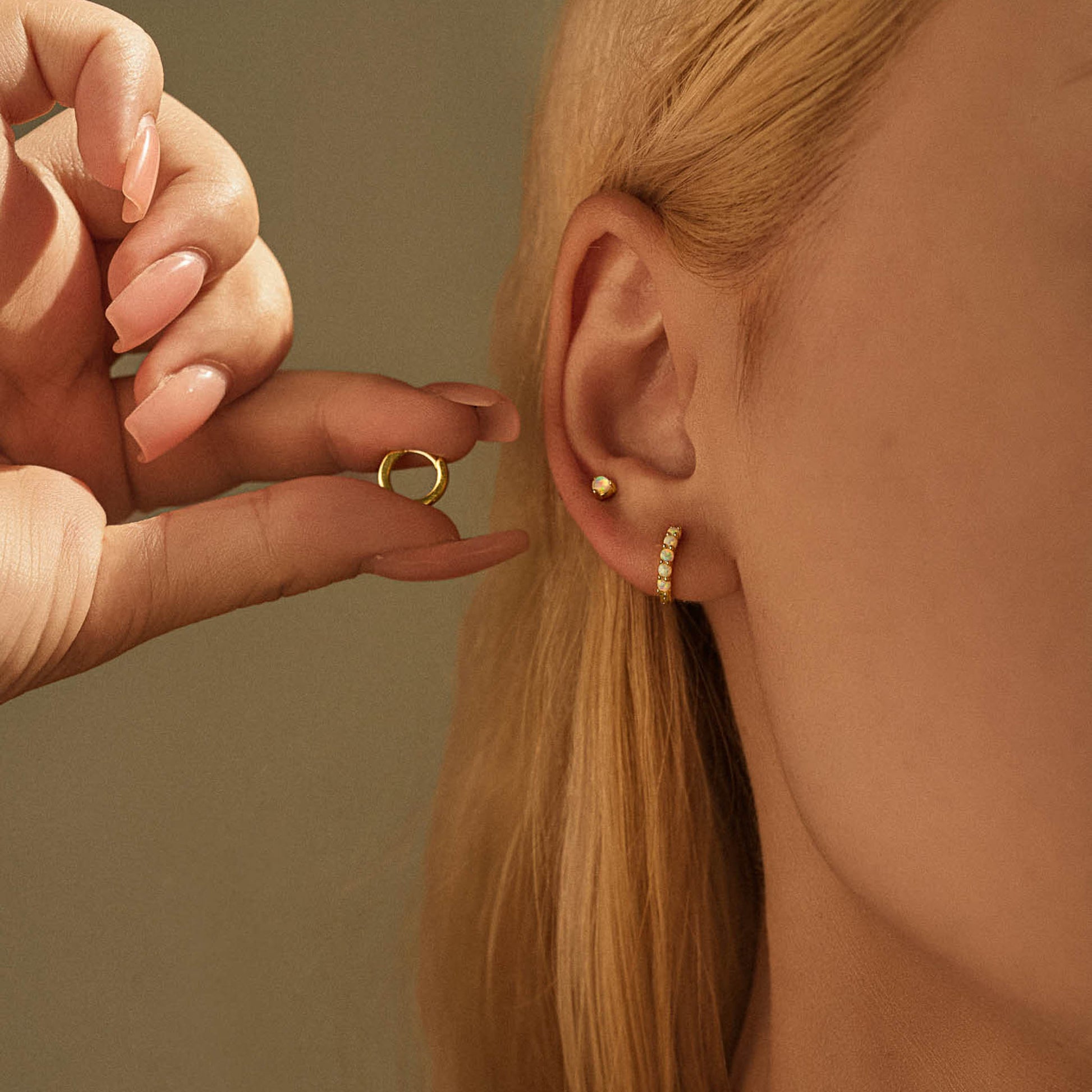 Model wearing gold plated opal stud and opal huggie hoop in a stacked ear, holding the plain huggie