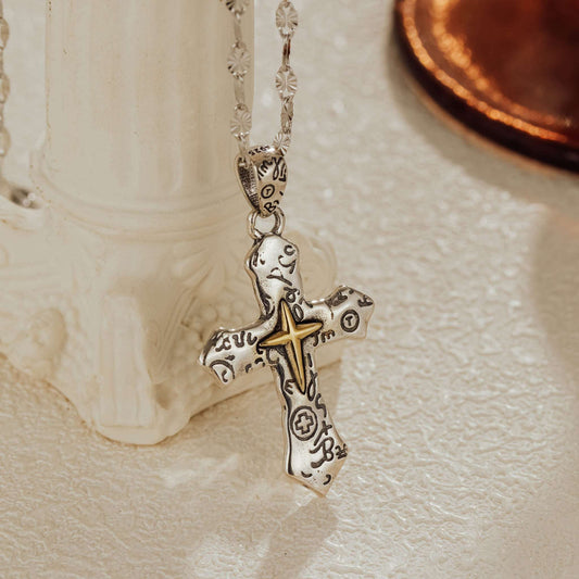 Close-up of oxidized sterling silver cross pendant with engraved detail, leaning against white vase