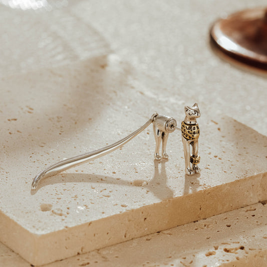 Egyptian cat two-tone sterling silver dangle earring with long tail on stone surface
