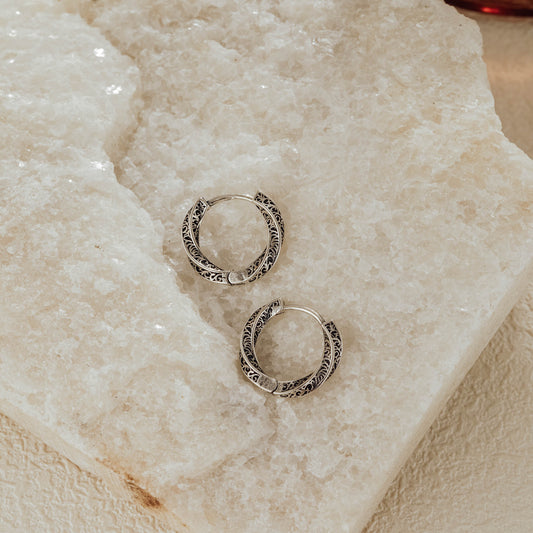 Oxidized sterling silver engraved huggie earrings displayed on crystal stone