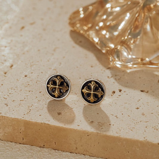 Pair of mini cross medallion two-tone sterling silver stud earrings on stone background