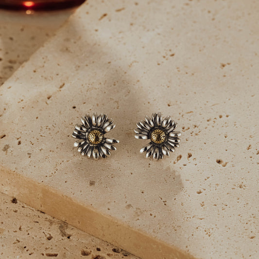 Pair of daisy two-tone sterling silver stud earrings with gold-tone brass centers on stone background